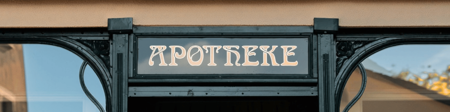Jugendstil-Schriftzug «Apotheke» über dem Eingang zur Beauty Apotheke in dunkelgrünem Rahmen.